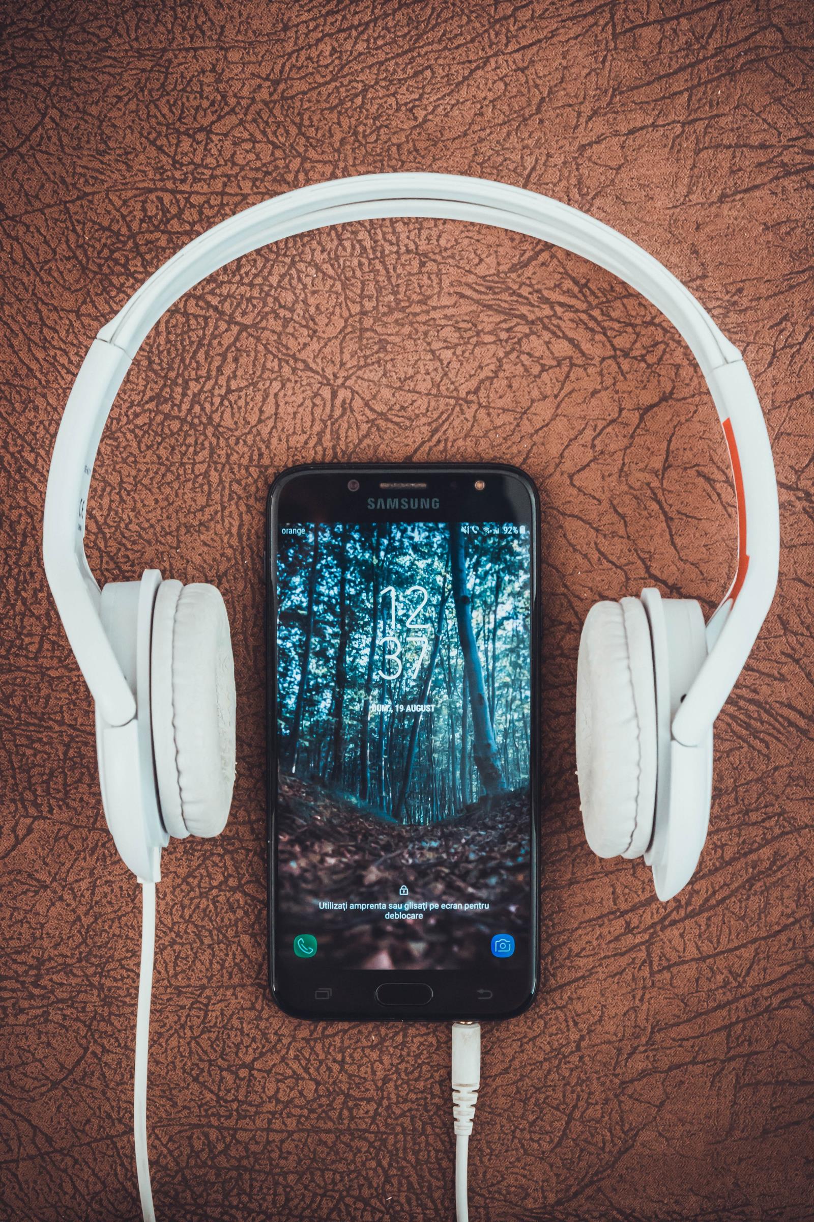 Over the ear white headphones plugged into a cell phone with the screen lit up Photo by Vlad Bagacian from Pexels